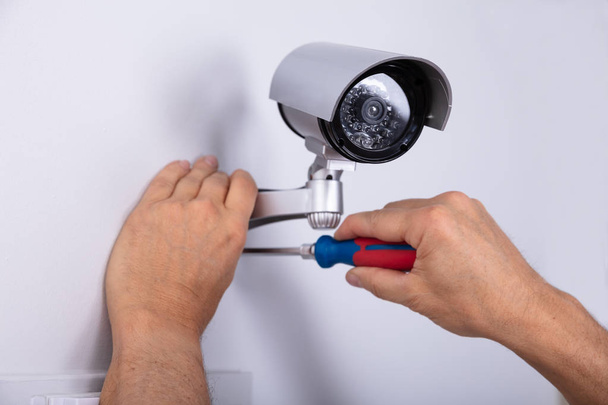 Close-up Of Male Technician Adjusting Cctv Camera On Wall With Screwdriver - Foto, afbeelding