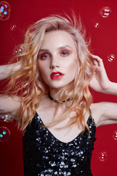 Portrait sexy fashion beautiful blonde woman with bright makeup posing on Red crimson background and soap bubbles. Slender blonde, perfect figure and long hair, soap bubbles. Clean perfect face skin - Foto, imagen