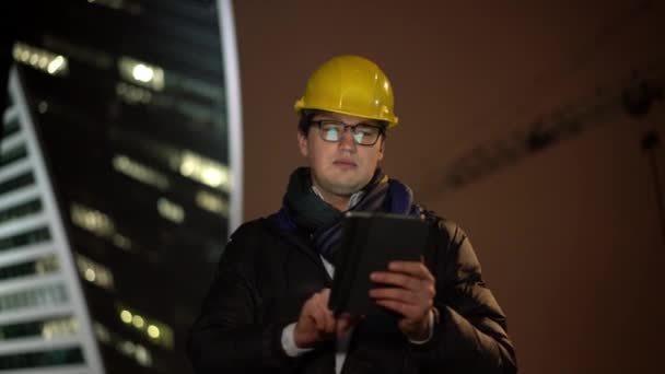 Medium shot of architect moving forward in yellow helmet holding a tablet - Кадры, видео