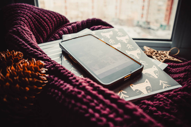 Phone and notepads on soft sweater on background of window - Zdjęcie, obraz