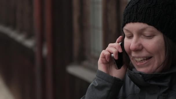 Mobil telefon beszélgetést, boldog, mosolygós felnőtt kaukázusi nő beszél a smartphone, az utcán, a hideg téli napon - Felvétel, videó