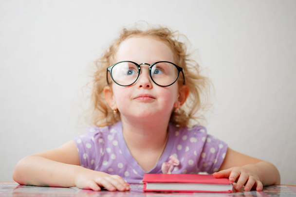 A little funny girl with glasses is going to read a book - Zdjęcie, obraz