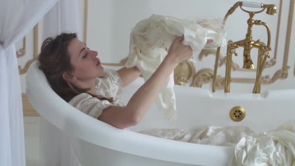 Young woman in white wedding dress lying in the amazing ampty bath, girl remove her hat with flowers and throwing in the air - Filmati, video
