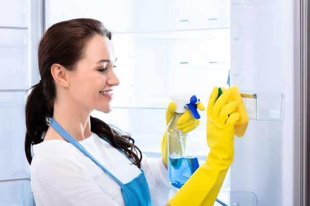 Rear View Of A Young Woman Wearing Gloves Cleaning Refrigerator With Sponge - Foto, immagini