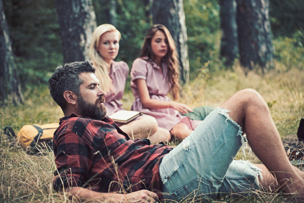 Man camping in forest with women on blurred background. Man with beard relax on grass. - Photo, Image