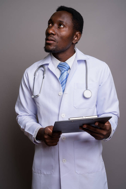 Jonge knappe Afrikaanse man arts tegen grijze achtergrond - Foto, afbeelding