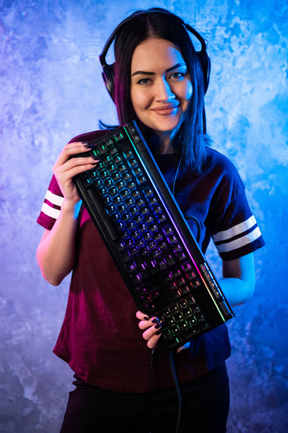 Beautiful Friendly Pro Gamer Streamer Girl posando con un teclado en sus manos, usando gafas. Atractiva chica geek con colores retro de neón fresco en el fondo. - Foto, imagen