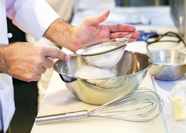 Baker sieving flour into a bowl in the kitchen of the bakery - Фото, изображение