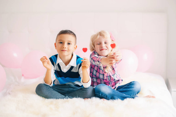 Group portrait of two happy white Caucasian cute adorable funny children eating heart shaped lollipops. Boy and girl celebrating Valentine Day. Love, friendship and fun. Best friends forever. - Фото, изображение