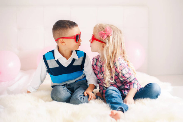 Portrait of two happy white Caucasian cute adorable funny children wearing heart shape glasses. Boy and girl trying to kiss each other. Love, friendship and fun. Valentine day holiday celebration. - Foto, Imagem