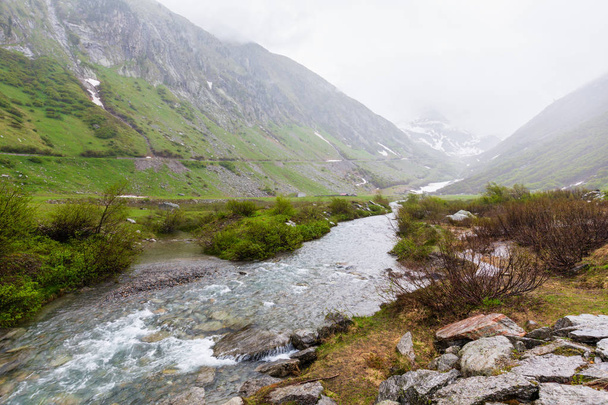 Passo del San Gottardo or St. Gotthard Pass summer misty landscape with water stream (Switzerland). Rainy weather. - Photo, Image