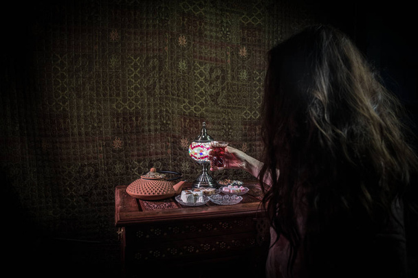 Copo de chá preto na mão da mulher em Low light lounge interior com tapete. Conceito de chá oriental. Lanches orientais na superfície de madeira vintage. Foco seletivo
 - Foto, Imagem