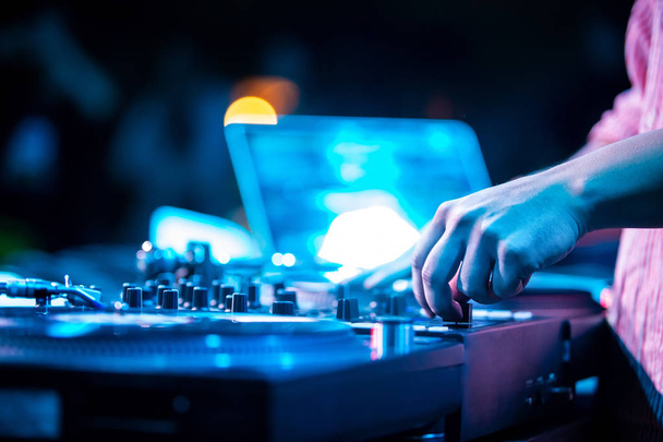 Hip hop party dj scratches vinyl records on turntable and cut tracks with cross fader knob on sound mixer.Professional disc jockey audio equimpent on stage in night club.Bright blue concert lights - Foto, imagen
