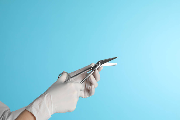 Female doctor holding bandage scissors on color background, closeup view with space for text. Medical object - Foto, Imagen