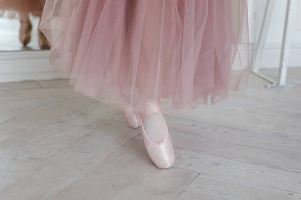 Manos de bailarina en falda tutú rosa se pone zapatos puntiagudos en pierna en salón de luz blanca. Joven bailarina de ballet clásica en clase de baile - Foto, Imagen
