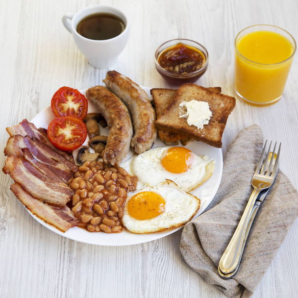 Повний англійський сніданок зі смаженими яйцями, ковбасками, беконом, бобами та тостами на білому дерев'яному фоні, вид збоку
. - Фото, зображення