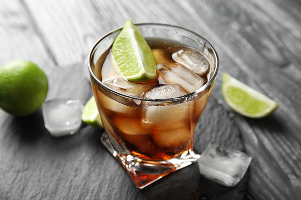 Glass of cocktail with cola, ice and cut lime on table - Foto, immagini