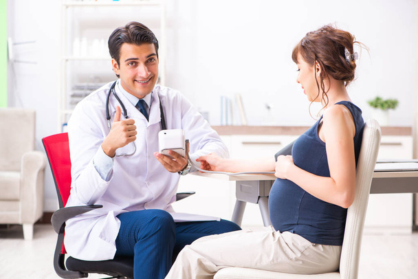 Young doctor checking pregnant womans blood pressure - Foto, imagen