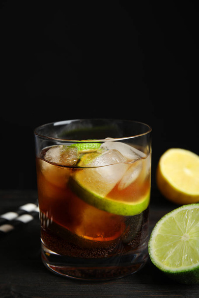 Glass of cocktail with cola, ice and cut lime on table against black background. Space for text - Фото, изображение