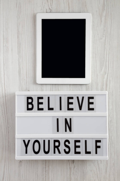 Modern board with text 'Believe in yourself', tablet on a white wooden background, top view. From above, flat lay, overhead.  - Foto, Imagem
