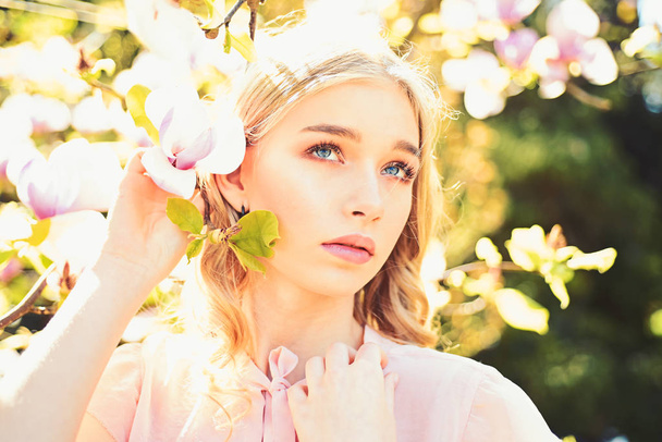 Girl on dreamy face, tender blonde near magnolia flowers, nature background. Spring bloom concept. Young woman enjoy flowers in garden. Lady walks in park on sunny spring day. - Фото, изображение