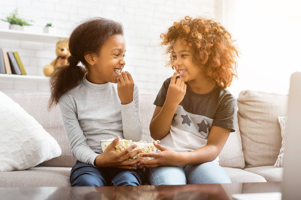 Afrikkalais-amerikkalaiset ystävät syövät popcornia, katsovat toisiaan, istuvat sohvalla kotona
 - Valokuva, kuva