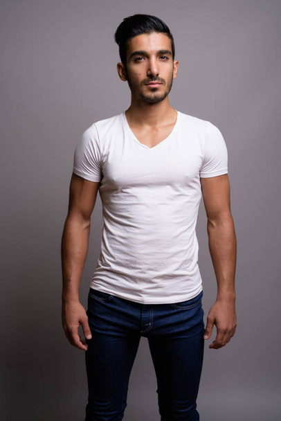 Young handsome Persian man against gray background - Valokuva, kuva