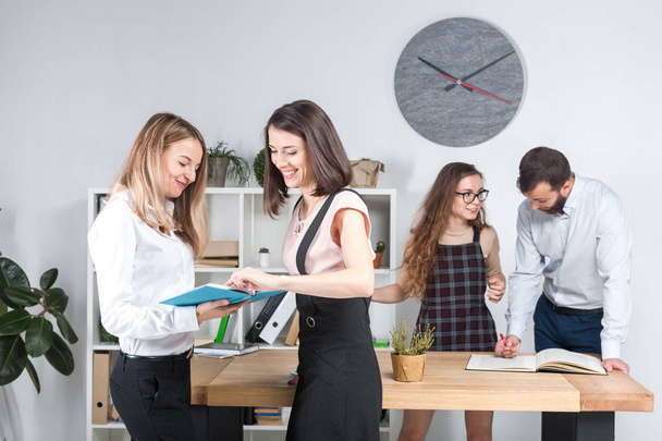 Themen Business, Teamwork und Verhandlungen im Büro. eine Gruppe von 4 kaukasischen Personen, die im Raum mit Dokumenten arbeiten. Zwei junge Frauen posieren vor dem Hintergrund von Firmenmitarbeiterinnen. - Foto, Bild