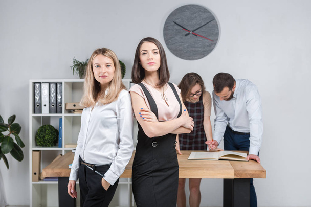 Themen Business, Teamwork und Verhandlungen im Büro. eine Gruppe von 4 kaukasischen Personen, die im Raum mit Dokumenten arbeiten. Zwei junge Frauen posieren vor dem Hintergrund von Firmenmitarbeiterinnen. - Foto, Bild