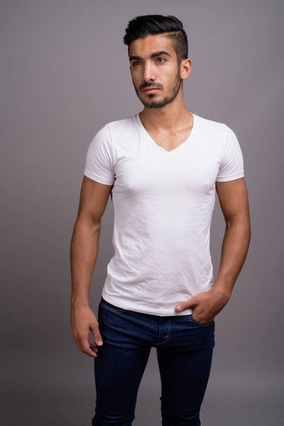 Young handsome Persian man against gray background - Fotó, kép