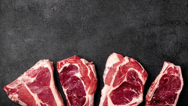 Meat raw steak lies on a black background. side view, copy space, top view - Zdjęcie, obraz