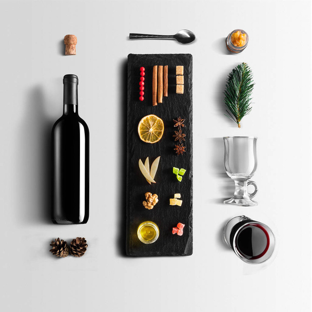 Mulled wine recipe ingredients and kitchen accessories, bottle of red wine, cinnamon, anise stars, orange, brown sugarand spice on gray background. - Photo, image
