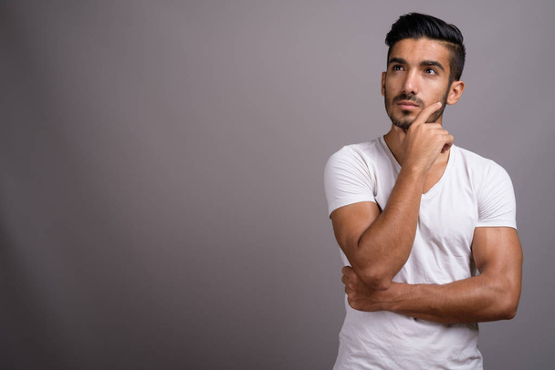 Young handsome Persian man against gray background - Foto, afbeelding