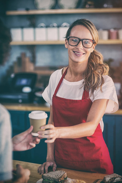 Portrait of waitress serving a coffee to customer at counter in cafe  - Foto, imagen