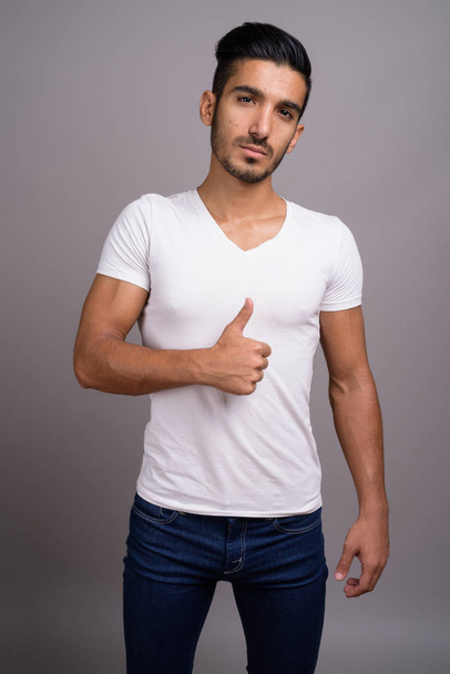 Young handsome Persian man against gray background - Foto, Imagem