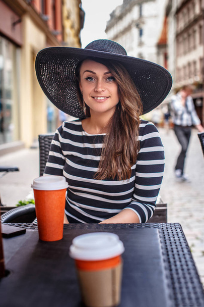 Porträt einer lächelnden Frau mit Kleid und stylischem Hut in einem Straßencafé im Sommer. - Foto, Bild