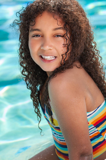 Biracial African American happy smiling young girl child relaxing on the side of a swimming pool  - Фото, зображення