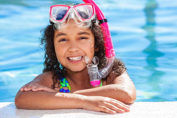 Biracial afroamericano feliz niña joven relajante en el lado de una piscina con gafas de color rosa y snorkel
 - Foto, imagen