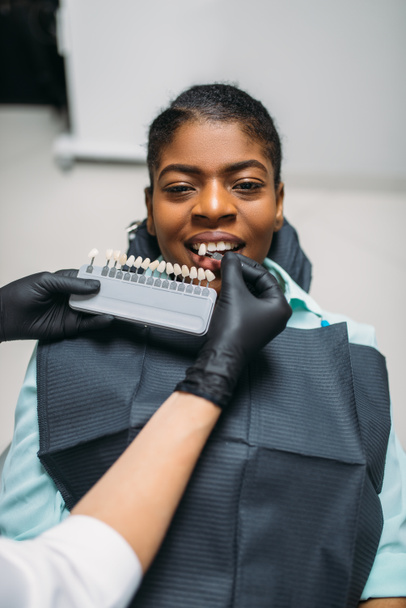 Οδοντίατρος επιλέγοντας την απόχρωση των δοντιών, θηλυκός ασθενής στο οδοντιατρείο. Γυναίκα στην οδοντιατρική αρχειοθήκη, Στοματολογία, φροντίδα των δοντιών - Φωτογραφία, εικόνα