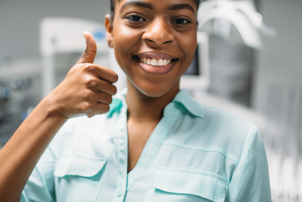 Smiling female patient shows thumbs up in dental clinic, medical equipment on background. Woman in dentistry cabinet, stomatology, teeth care - Photo, Image