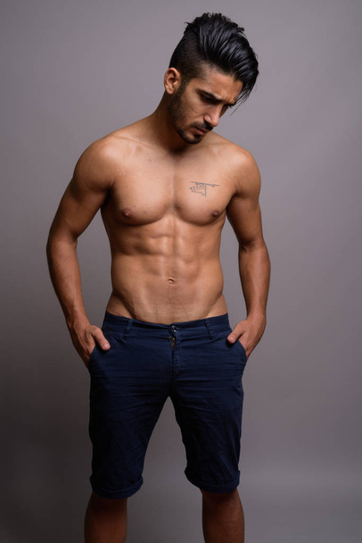 Young handsome Persian man shirtless against gray background - Fotó, kép