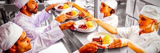 Chefs passing ready food to waiter at order station in commercial kitchen - 写真・画像