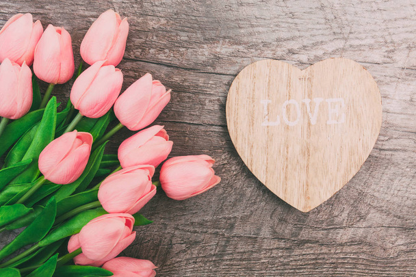 Bouquet of pink tulips and a valentine in the shape of a heart from wood, on a wooden background. Valentine's Day - Photo, image