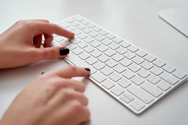 Primo piano di mani femminili sfocate che digitano sulla tastiera bianca che sta lavorando in ufficio e usando il computer
 - Foto, immagini