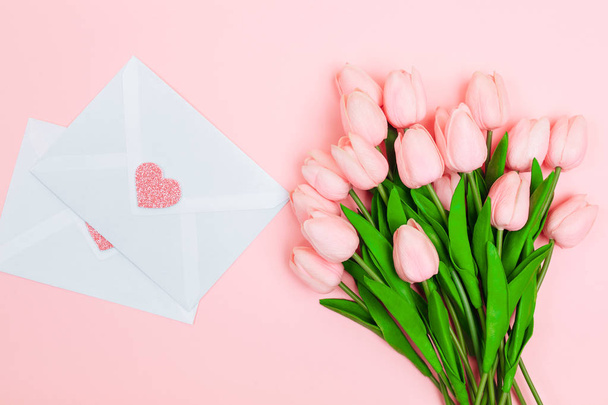 Female hands with a bouquet of pink tulips and blank white letter envelopes, on a pink background. View from above. women's Day - 写真・画像