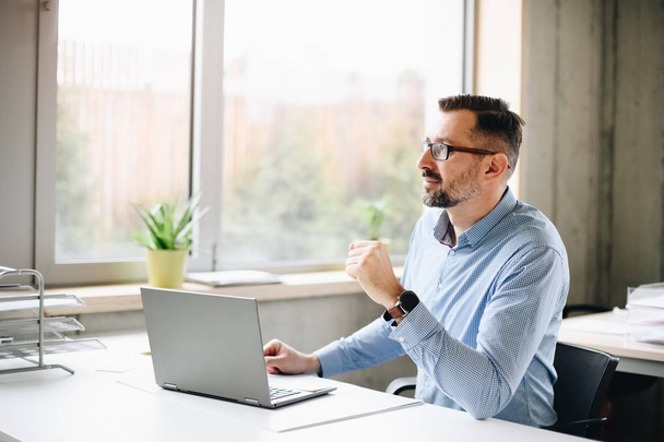 Midden leeftijd knappe man in shirt op laptopcomputer in kantoor werkt. Man aan het werk op kantoor - Foto, afbeelding