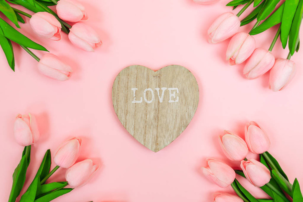 Spring pink tulips and a wooden valentine in the shape of a heart, on a pink background. Women's Day - Fotó, kép