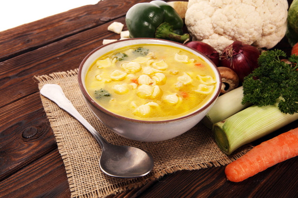 Heldere soep met kip en noedels. Bouillon met wortelen, uien diverse verse groenten in een pot. - Foto, afbeelding