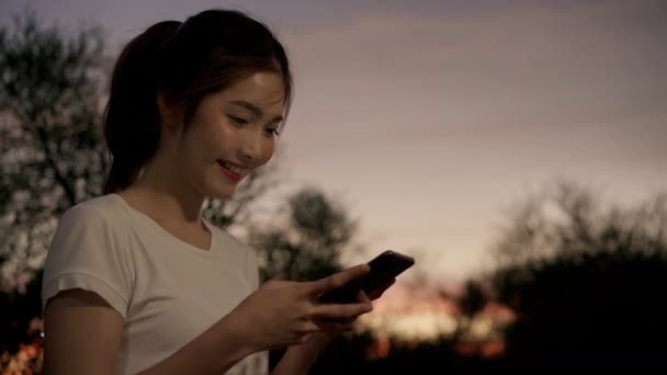fröhliche asiatische Touristenbloggerin mit Touchscreen-Technologie am Smartphone, während sie nachts auf der Straße in der Innenstadt spaziert. Lifestyle Rucksack touristisches Reisekonzept. - Filmmaterial, Video