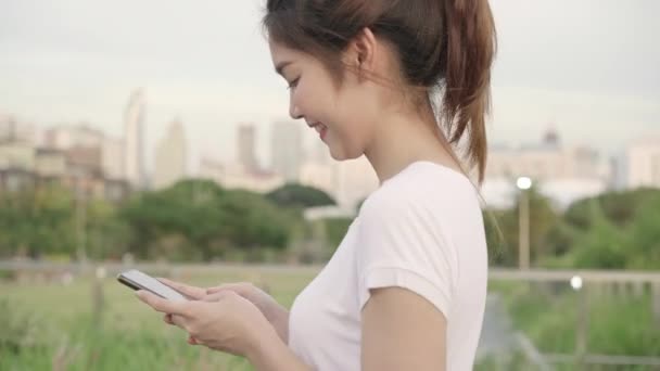 Joyeux asiatique blogueuse touristique femme en utilisant la technologie de l'écran tactile au smartphone tout en marchant dans la rue au centre-ville le soir. Lifestyle sac à dos touristique Voyage concept de vacances
. - Séquence, vidéo